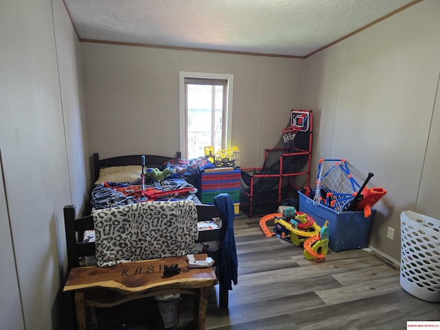 bedroom featuring crown molding, a textured ceiling, a decorative wall, and wood finished floors