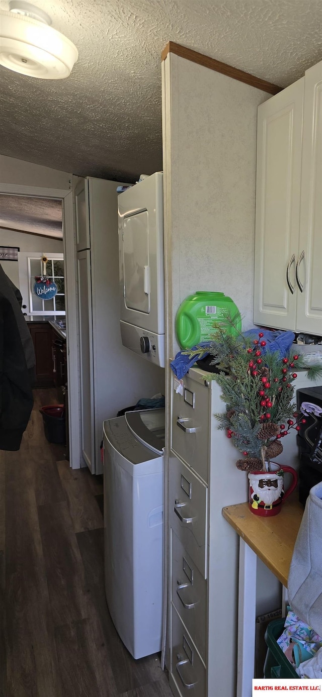 clothes washing area featuring cabinet space, a textured ceiling, stacked washer / dryer, and dark wood-type flooring