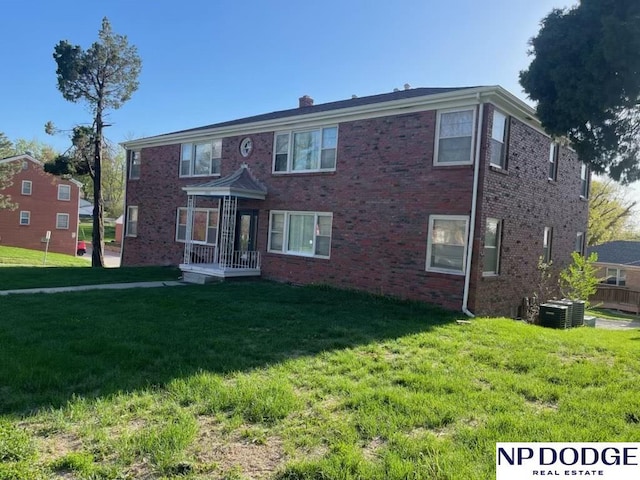 view of front of house featuring central AC unit, a chimney, brick siding, and a front yard