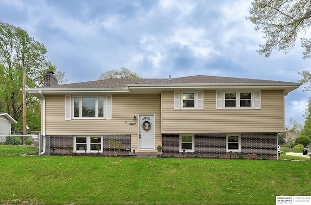 raised ranch featuring a chimney, brick siding, entry steps, fence, and a front yard