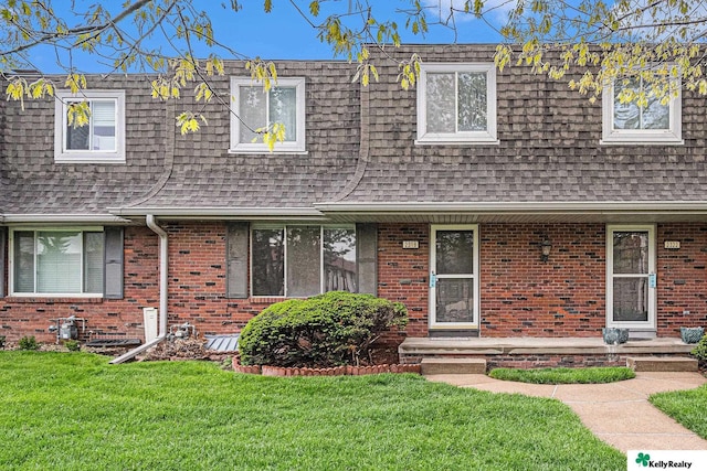 view of front of property with mansard roof, a front yard, brick siding, and a shingled roof
