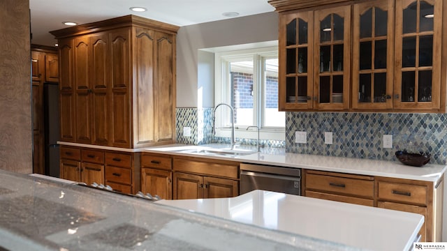 kitchen with dishwasher, a sink, glass insert cabinets, backsplash, and brown cabinets