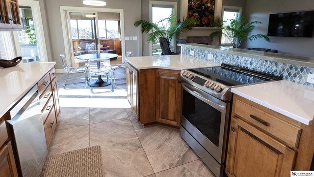 kitchen with appliances with stainless steel finishes, brown cabinets, light countertops, a fireplace, and open floor plan