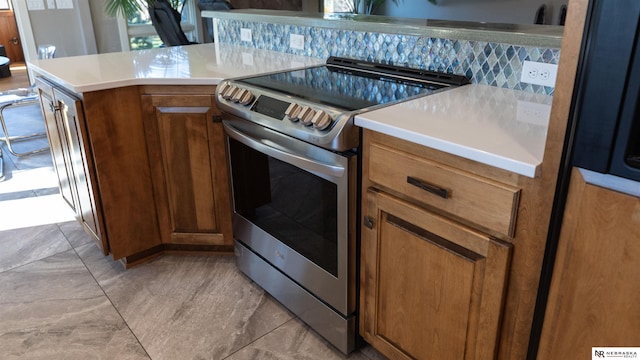 kitchen with stainless steel electric range oven, brown cabinetry, light countertops, and tasteful backsplash