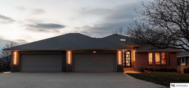 prairie-style home featuring an attached garage, brick siding, driveway, and a shingled roof