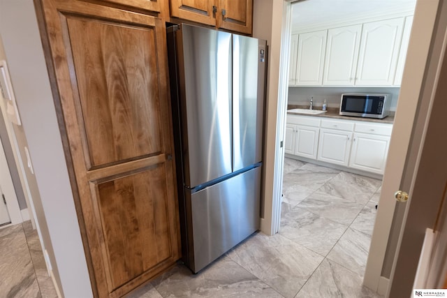 kitchen with stainless steel appliances, light marble finish flooring, a sink, and white cabinetry