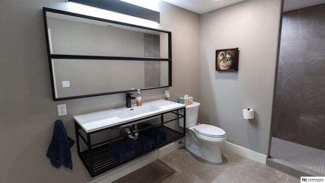 bathroom with toilet, a tile shower, baseboards, and vanity