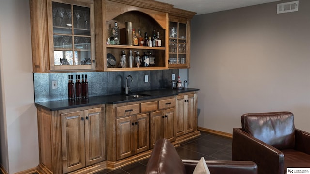 indoor wet bar featuring decorative backsplash, dark tile patterned flooring, and baseboards