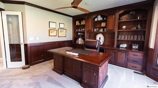 home office with light colored carpet, ornamental molding, wainscoting, a ceiling fan, and built in study area