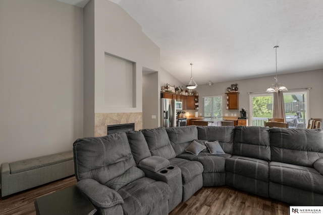 living room featuring a tiled fireplace, dark wood-type flooring, lofted ceiling, and a notable chandelier