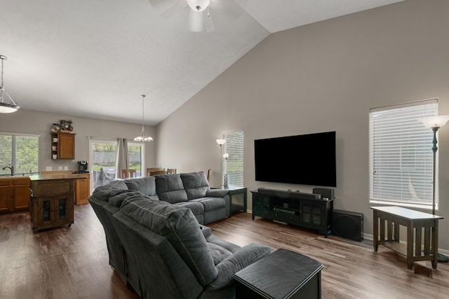 living area featuring dark wood-style floors, ceiling fan with notable chandelier, high vaulted ceiling, and baseboards