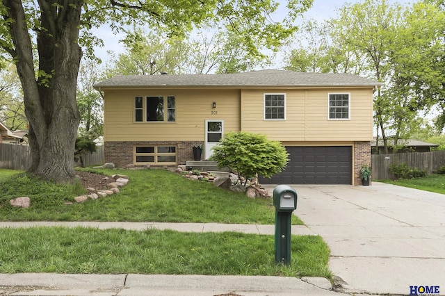 raised ranch with a garage, fence, concrete driveway, a front yard, and brick siding