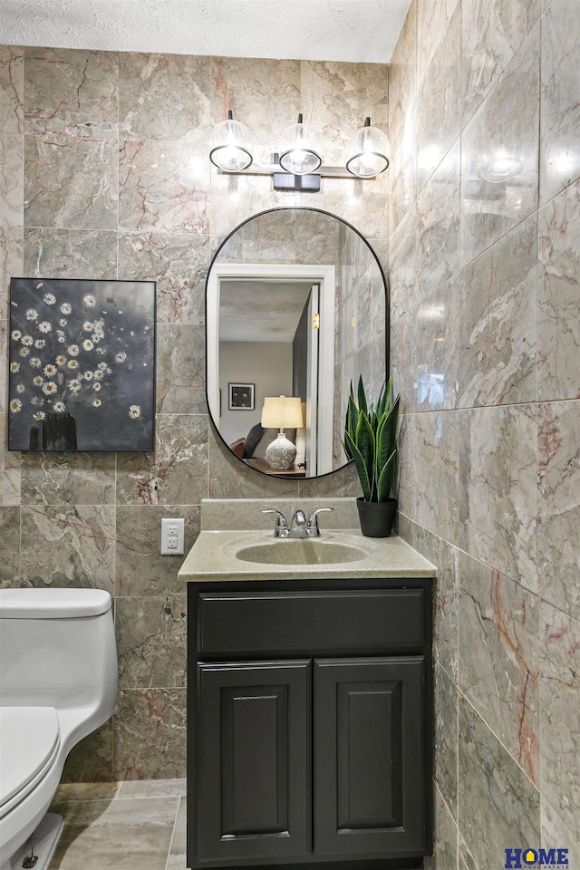 half bathroom with vanity, tile walls, a textured ceiling, and toilet