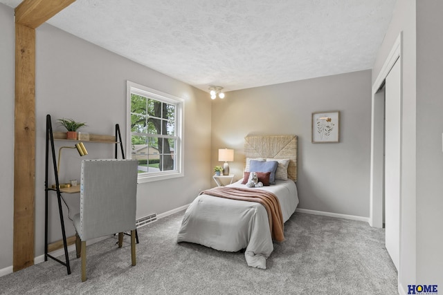 carpeted bedroom with a textured ceiling, baseboards, and a closet