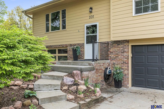 doorway to property featuring concrete driveway, brick siding, and an attached garage