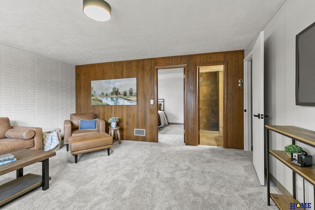sitting room with a textured ceiling, visible vents, wooden walls, carpet flooring, and brick wall