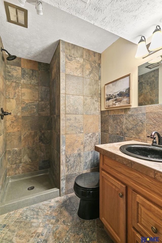 full bathroom with toilet, tile walls, stone finish floor, and tiled shower