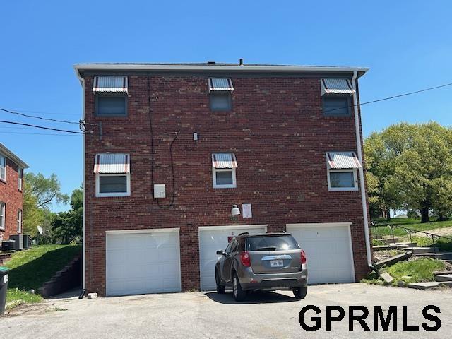 back of house featuring an attached garage, brick siding, and driveway