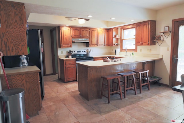 kitchen with under cabinet range hood, a kitchen bar, a peninsula, light countertops, and appliances with stainless steel finishes