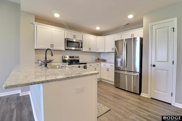 kitchen featuring a sink, a peninsula, stainless steel appliances, visible vents, and light wood-style flooring