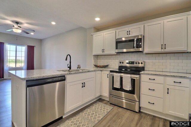 kitchen with a ceiling fan, light wood-style flooring, a sink, a peninsula, and appliances with stainless steel finishes