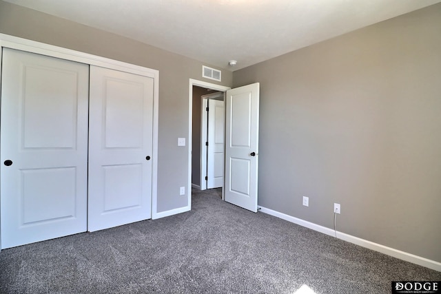 unfurnished bedroom featuring baseboards, dark carpet, a closet, and visible vents