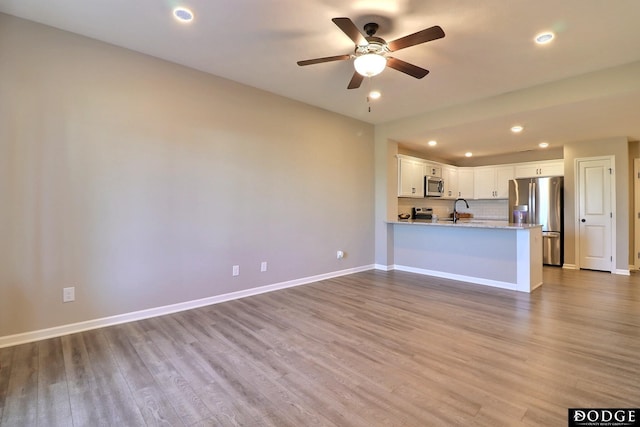unfurnished living room with a sink, wood finished floors, recessed lighting, ceiling fan, and baseboards