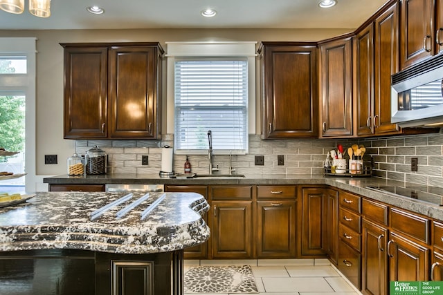 kitchen with stainless steel microwave, a sink, tasteful backsplash, light tile patterned floors, and black electric cooktop