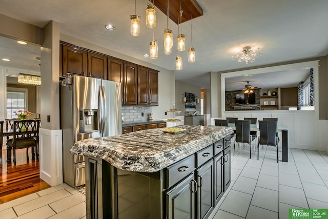 kitchen with light tile patterned floors, dark brown cabinets, dark stone countertops, stainless steel appliances, and decorative backsplash