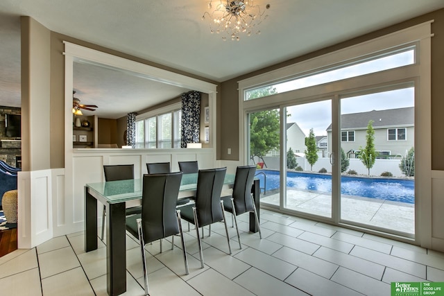dining room with a decorative wall, ceiling fan with notable chandelier, a wainscoted wall, and light tile patterned floors