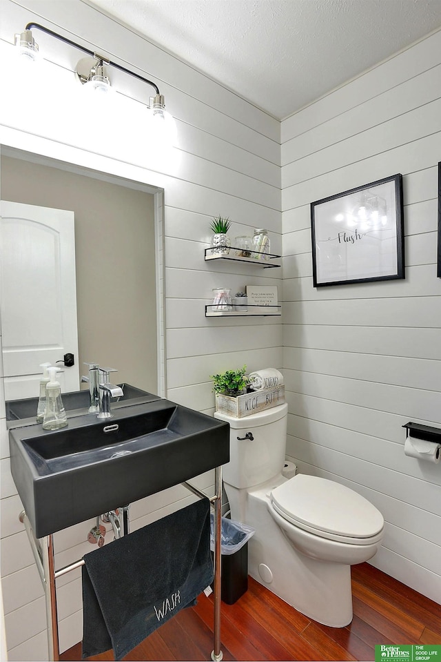 half bath with toilet, wood walls, and wood finished floors