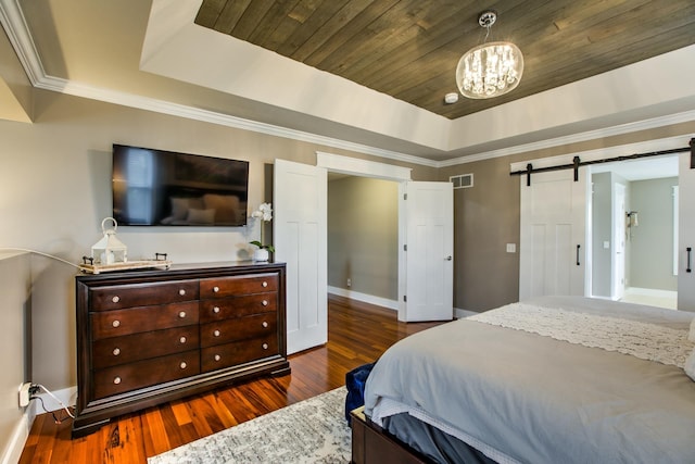 bedroom with a raised ceiling, a barn door, visible vents, and wood finished floors