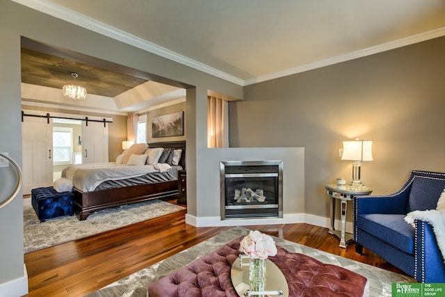 bedroom with wood finished floors, ornamental molding, a barn door, baseboards, and a glass covered fireplace