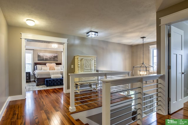corridor with an inviting chandelier, a wealth of natural light, dark wood-style floors, and an upstairs landing