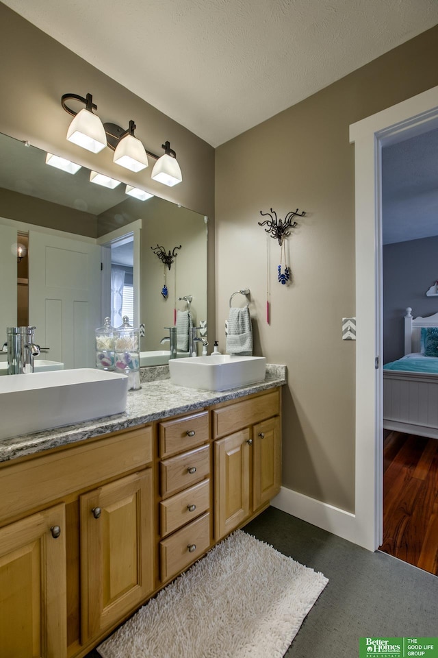 ensuite bathroom featuring a sink, double vanity, ensuite bathroom, and baseboards