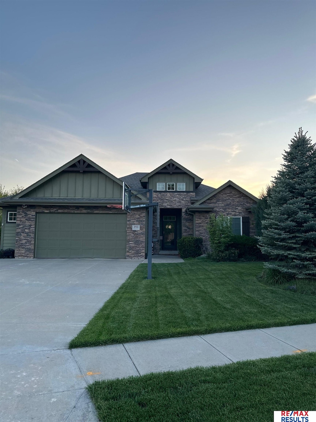 prairie-style house featuring stone siding, an attached garage, a front lawn, board and batten siding, and driveway