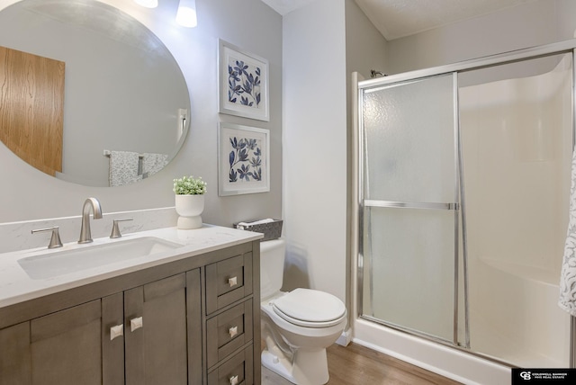 bathroom with vanity, toilet, wood finished floors, and a stall shower