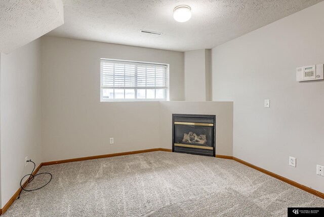 unfurnished living room with carpet, a textured ceiling, visible vents, baseboards, and a glass covered fireplace