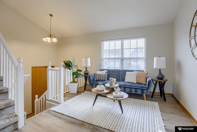 living area featuring lofted ceiling, light wood-type flooring, stairway, an inviting chandelier, and baseboards