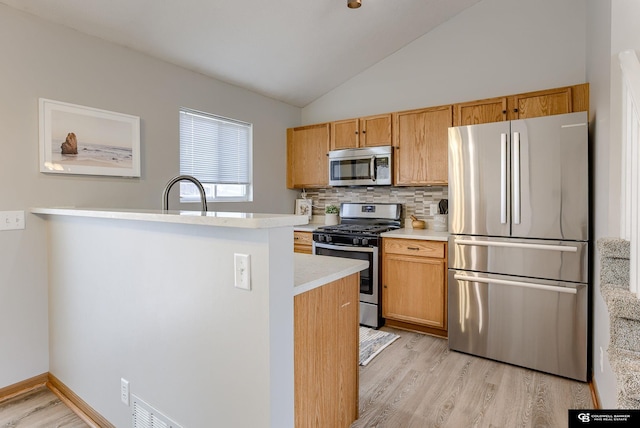 kitchen with light wood finished floors, stainless steel appliances, backsplash, and light countertops