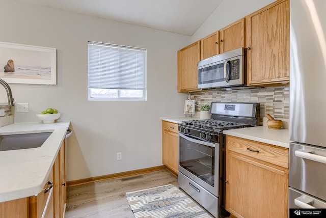 kitchen featuring light wood-style floors, stainless steel appliances, a sink, and backsplash