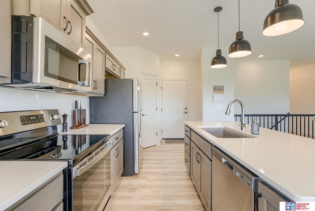 kitchen featuring a sink, stainless steel appliances, decorative light fixtures, light wood finished floors, and light countertops