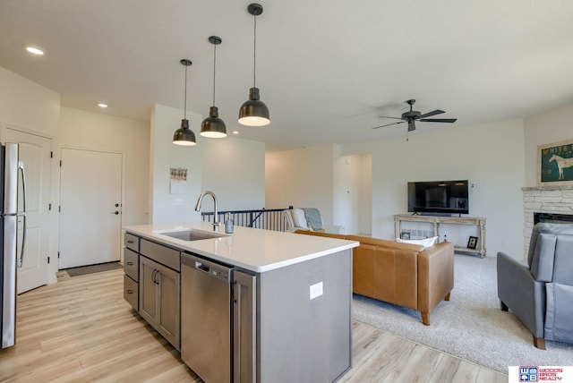 kitchen with a ceiling fan, a sink, open floor plan, light wood-style floors, and stainless steel appliances