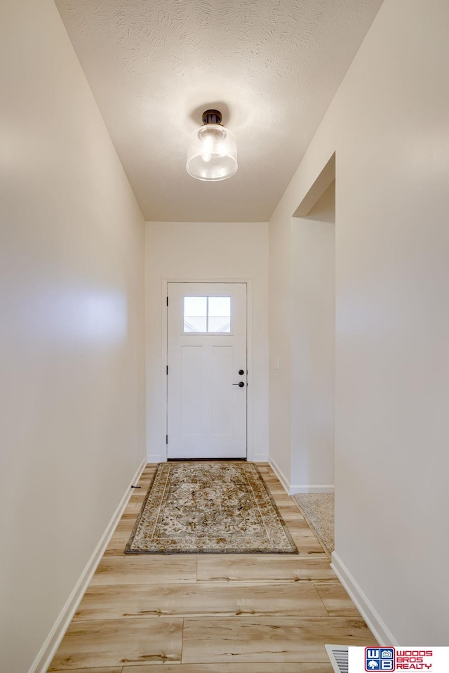 doorway with baseboards, light wood-style flooring, and a textured ceiling