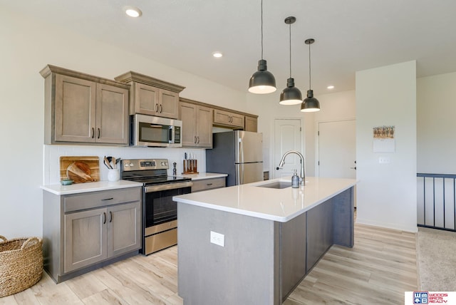 kitchen featuring a sink, light wood-type flooring, a center island with sink, backsplash, and appliances with stainless steel finishes
