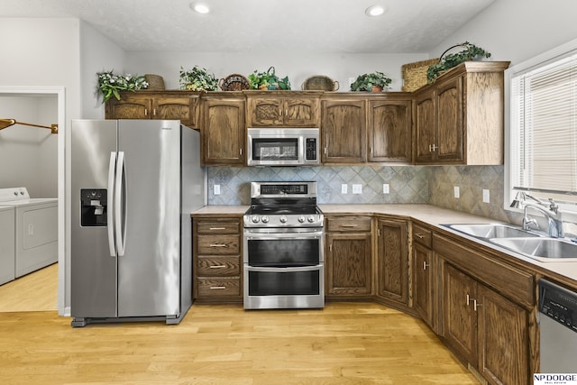 kitchen with light wood finished floors, a sink, stainless steel appliances, independent washer and dryer, and decorative backsplash