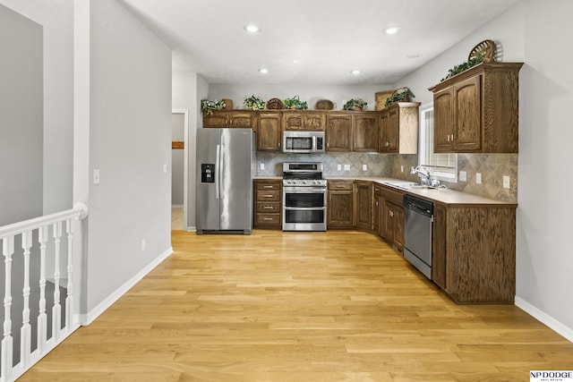 kitchen featuring a sink, stainless steel appliances, backsplash, and light wood-style flooring