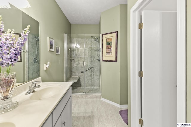 bathroom with a stall shower, baseboards, double vanity, and a sink