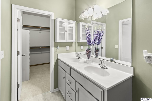 bathroom with baseboards, a spacious closet, double vanity, and a sink