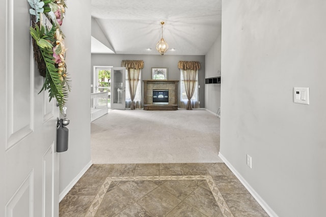 interior space featuring carpet flooring, vaulted ceiling, baseboards, a glass covered fireplace, and a chandelier